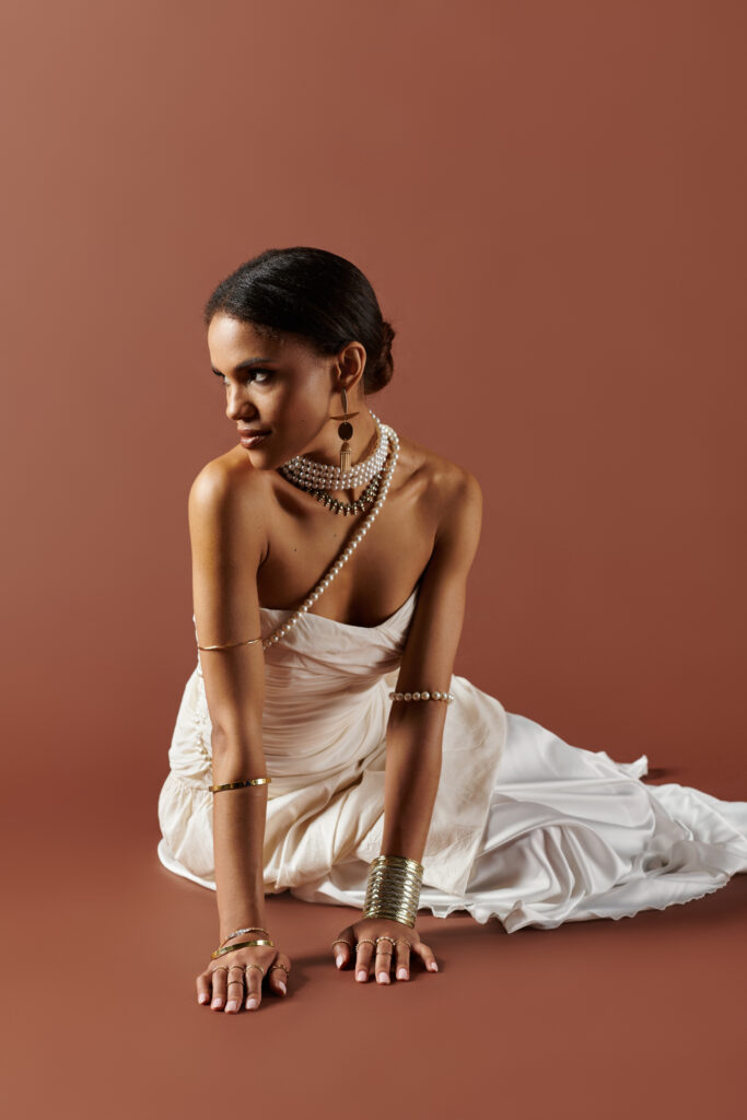 Elegant caramel skinned women sitting and wearing a white dress and pearl accessories